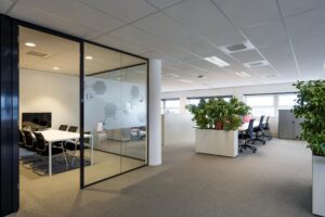 Moderne kantoorruimte aan de H.J.E. Wenckebachweg met glazen vergaderruimte, bureaus en veel groen.